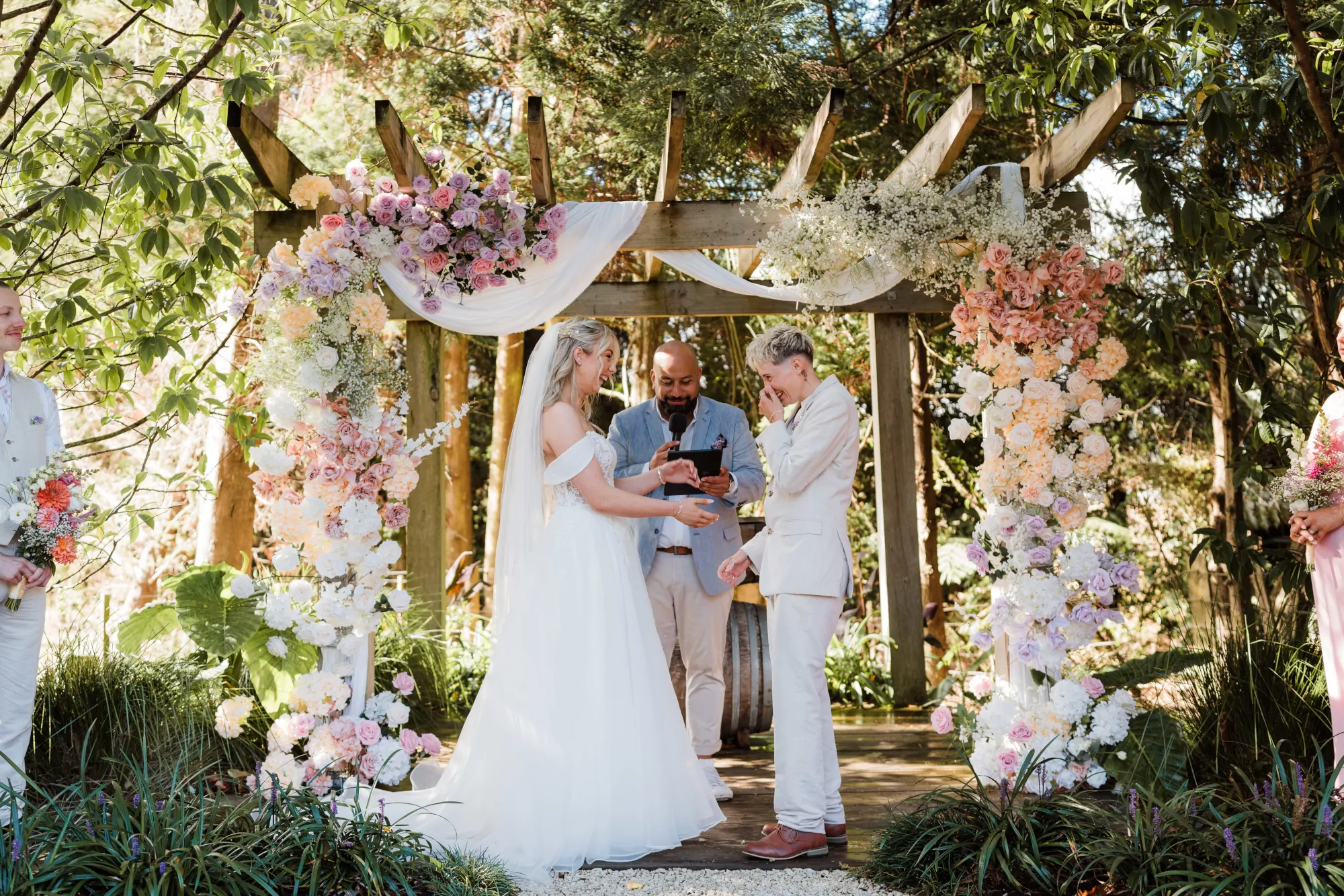 A Kiwi couple holding hands at their outdoor wedding ceremony